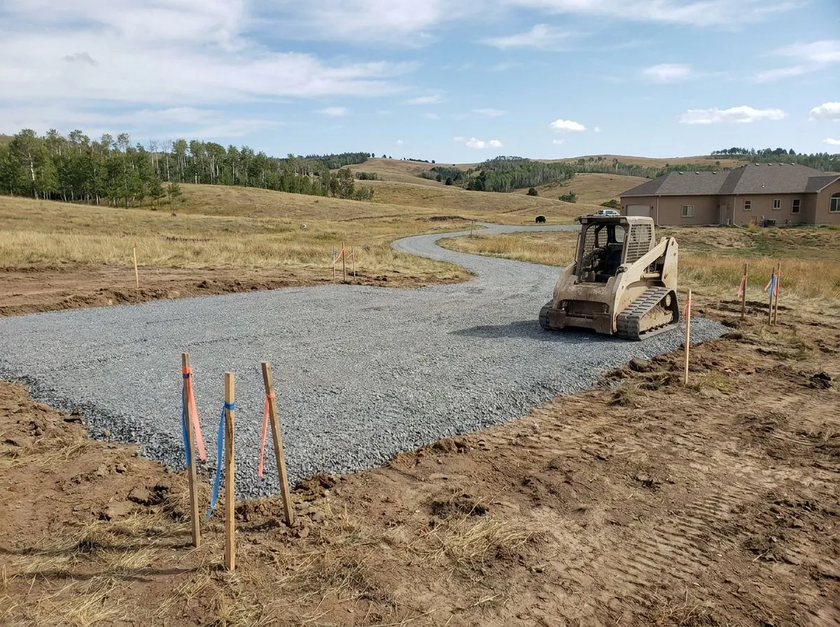 A levelled gravel pad for a new shop building on a rural acreage, with rolling foothills and aspen groves behind.